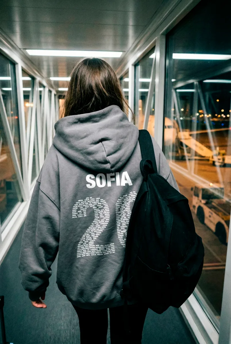 Chica de espaldas con prenda personalizada en el finger acristalado de un aeropuerto